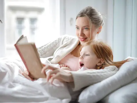 A mother and her daughter reading a book together in a bright bedroom