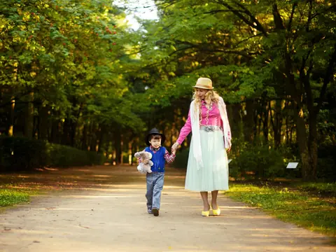 A mother and son walking hand in hand along a sunny park path