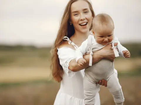 A happy mother lifting her baby in a sunny field