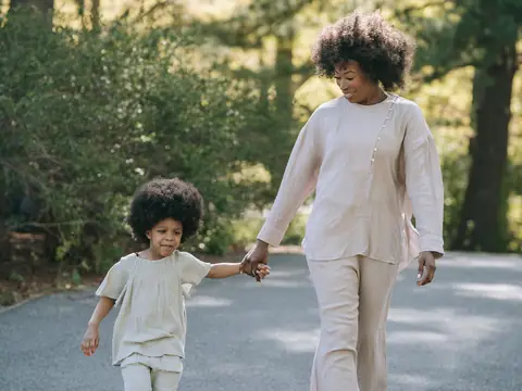 A mother and daughter walking hand in hand on a sunny tree-lined path