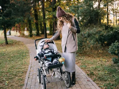 A mother walking with her baby in a stroller through a park in autumn